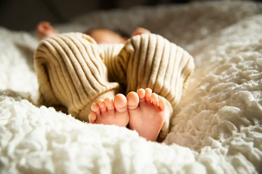Anonymous barefooted baby sleeping on soft bed in sunlight